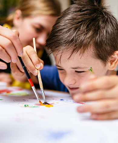 A young child painting with their social care worker